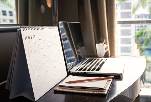 Desk calendar 2027 background with laptop computer and hot coffee cup on hotel office table for business planning design