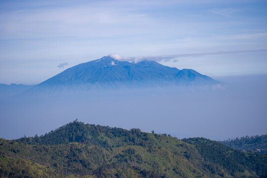 Majestic Mount Arjuno rises through a thick blanket of fog, with golden hills stretching across the landscape in a stunning East Java sunrise scene.