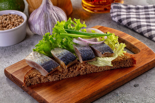 Salted herring appetizer on dark rye bread with lettuce and onions on a wooden board