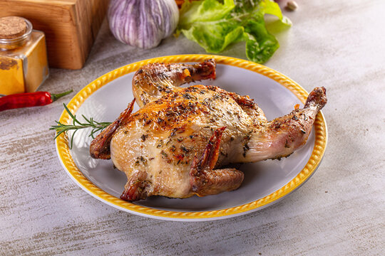Gourmet roasted whole quail seasoned with herbs on a rustic kitchen table.