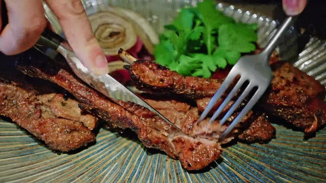 Close up of hands cutting delicious grilled lamb chops with knife and fork on a plate with garnish.