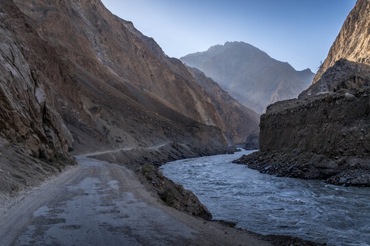Pamir Highway winding along a rushing river through steep rocky canyons in the remote mountainous region of Afghanistan under Taliban control.
