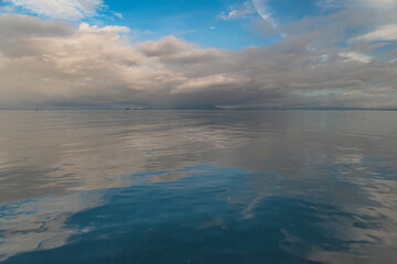 Obraz premium Peaceful seascape featuring calm water reflecting clouds beneath a bright blue sky