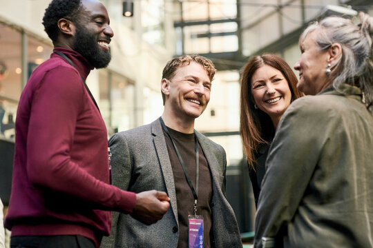 Smiling male and female business professionals talking with senior executive at networking event in convention center