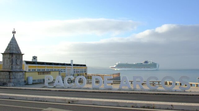 04 June 2026, Portugal, Paco de Arcos - Cruise ship arrives at Paco de Arguero in morning light, busy scenes by the shore. ship docks at harbor. cars pass by water. sky bright.  lively spot in morning