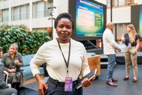 Portrait of female business entrepreneur holding diary standing in lobby for networking event at convention center