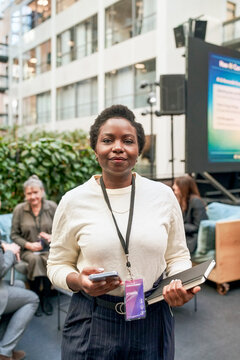 Portrait of female entrepreneur holding diary and smart phone while standing in lobby for networking event at convention