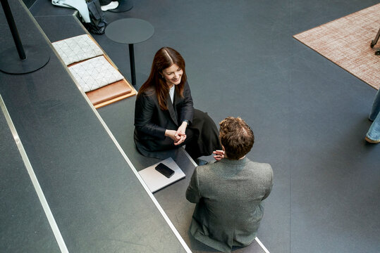 High angle view of smiling mature businesswoman listening to male expert while sitting on step in networking event at co