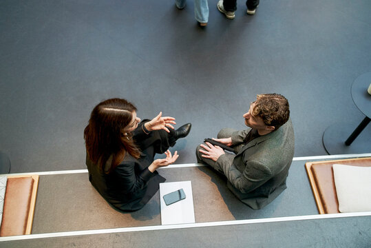 High angle view of mature businesswoman discussing ideas with male expert while sitting on step in networking event at c
