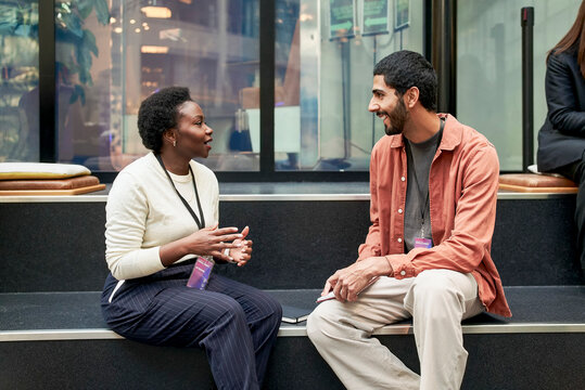 Smiling male entrepreneur listening to ideas of female executive while sitting on steps in networking event