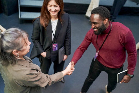 High angle view of smiling male entrepreneur greeting senior female business expert at corporate event in convention cen