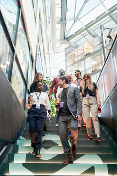 Low angle view of male and female business experts talking with each other while moving down on stairs in convention cen