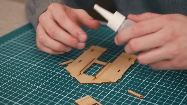 Securing wooden miniature house details with glue during model assembly. DIY architecture crafting featuring plywood component installation and precision home construction workflow. Creative