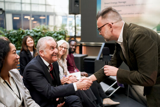 Mature male keynote speaker shaking hands with senior business executive while interacting during seminar in convention