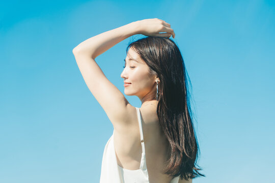 青空背景の夏服の若い女性