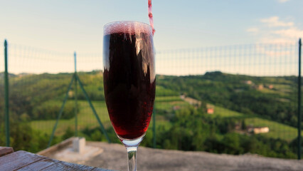 Obraz premium Red Wine Pouring into Glass with Scenic Italian Vineyard Background