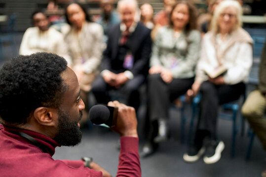 High angle view of mature male keynote speaker using microphone while addressing audience at business seminar
