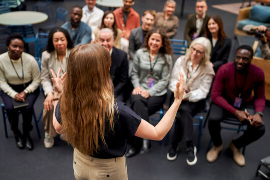 High angle rear view of long haired female speaker gesturing with hands while communicating with audience in convention