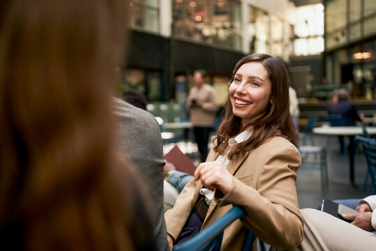 Smiling female business professional looking over shoulder while talking with associate at seminar in convention center