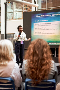 Female presenter speaking into microphone while explaining how AI can help solve energy crisis during seminar in convent