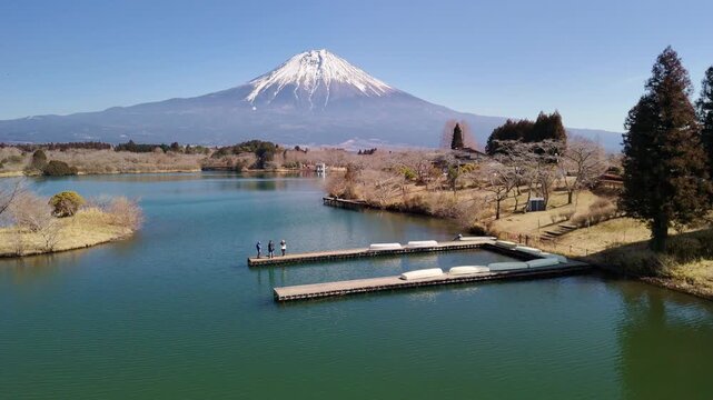Aerial shot flying towards a wooden lake dock with tourists, framed by the breathtaking snow-capped peak of Mount Fuji.