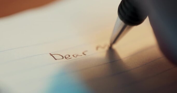 A detailed macro shot showing a pen writing the words Dear Mom on a white notebook, highlighting the personal touch of a handwritten letter.