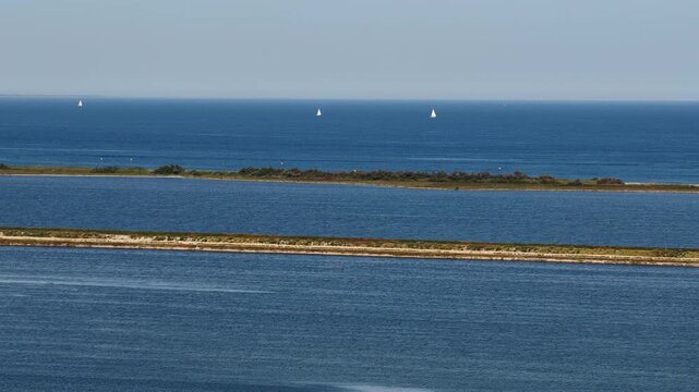 Sailboats on blue Mediterranean Sea beyond narrow sandbars and lagoon, France