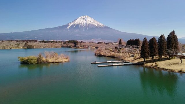 Smooth drone reverse shot pulling back across a green lake to reveal a wide, majestic panoramic view of Mount Fuji.