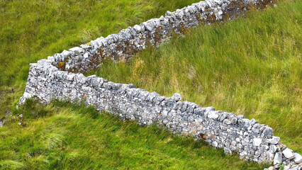 Aerial View of Ancient Stone Wall in Green Scottish Grassland © blueringmedia