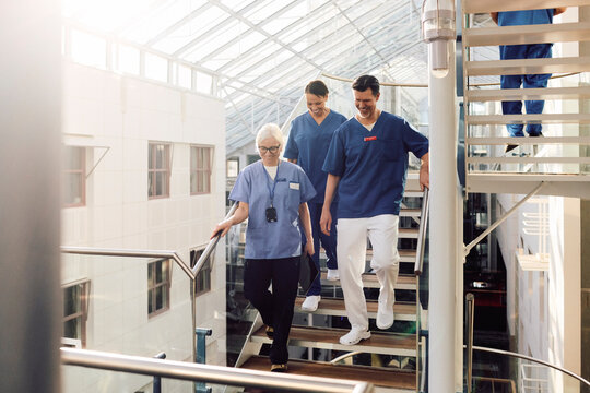 Smiling male and female medical professionals moving down on steps in hospital building