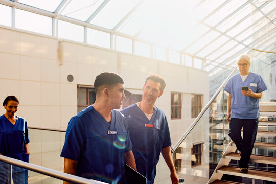 Multiracial male healthcare professionals talking with each other while walking in hospital corridor
