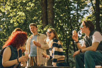 Obraz premium Cheerful young friends with ice cream laughing in park with retro effect. Concept of weekend joy, candid emotions, outdoor gathering, summer leisure, and friendly conversation.