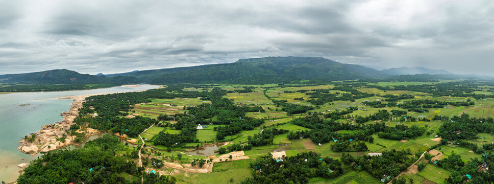 Aerial view of the lush green landscape with a winding river and distant hills under a cloudy sky in Sunamganj, Sylhet Division, Bangladesh.