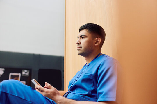 Young male healthcare expert spending break time with smart phone while sitting in hospital lobby