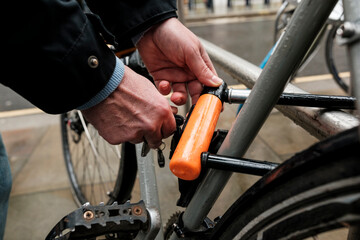 Fototapeta premium Hands locking u-lock securing bicycle to city rack
