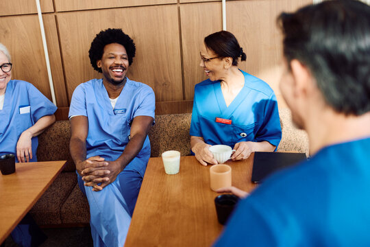 Happy male physician enjoying coffee break with team in hospital cafeteria