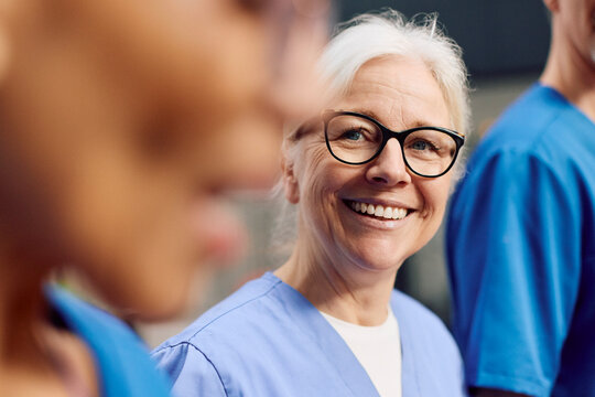 Smiling senior female physician wearing eyeglasses talking with colleague