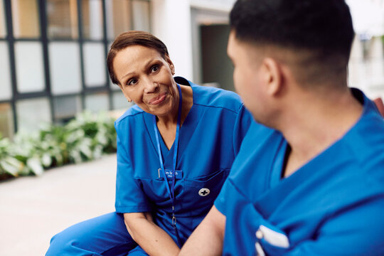 Smiling senior female physician consoling male coworker while sitting in hospital lobby
