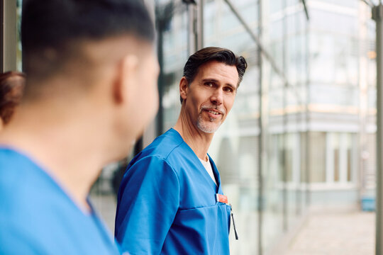 Mature male physician spending leisure time with colleague during break outside hospital building