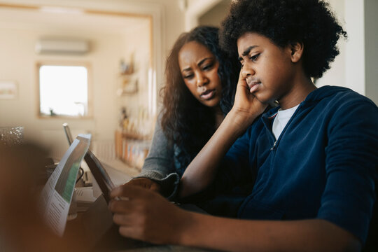 Mother helping son while doing studies on tablet PC at home