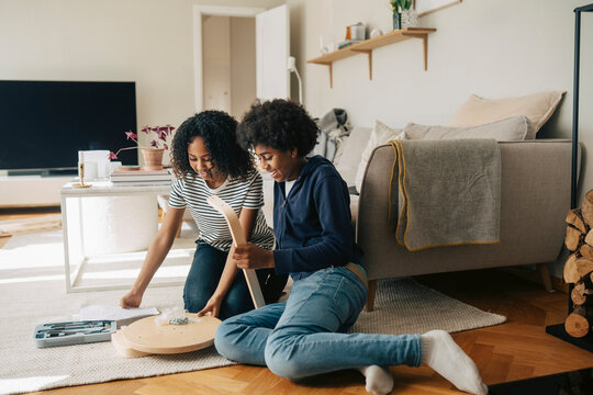 Smiling siblings building DIY furniture while sitting on floor at home