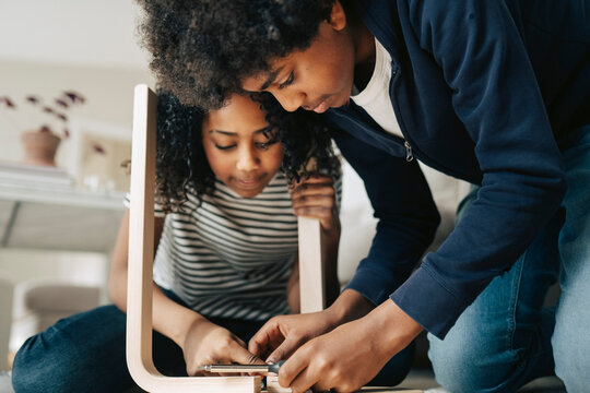 Brother and sister helping each other while assembling furniture at home