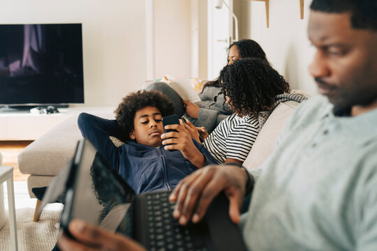 Children spending leisure time using smart phones while relaxing on sofa with family at home