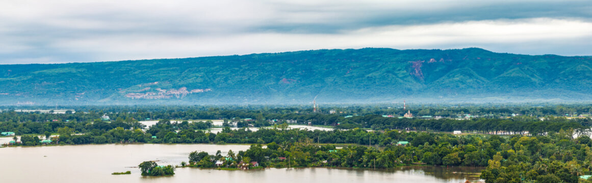 Aerial view of lush green landscapes and flooded plains with dense trees and blue hills under a cloudy sky in Sunamganj, Sylhet Division, Bangladesh.