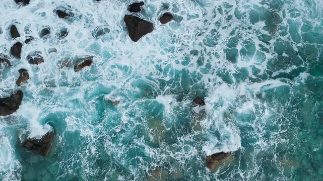 Turquoise Atlantic water with wave foam moving around rocks. Aerial view of coastal reef and natural marine texture