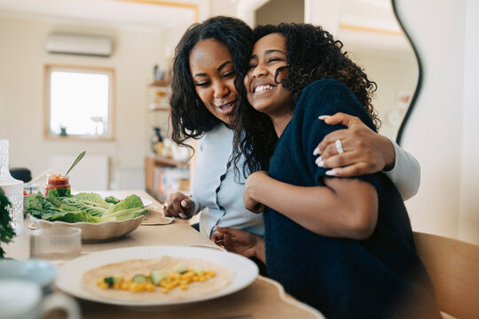 Woman embracing daughter sitting at dining table during lunch time