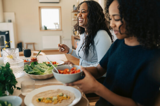 Happy woman eating lunch while sitting next to daughter at home
