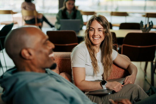 Diverse colleagues laughing during conversation while sitting on couch at coworking space
