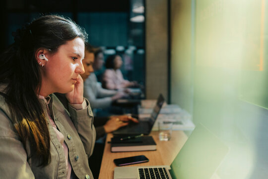 Businesswoman adjusting wireless in-ear headphones while doing video call on laptop at office