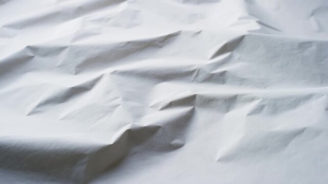 Slow pan close up of crumpled white paper texture shifting on studio tabletop with subtle light and shadow study